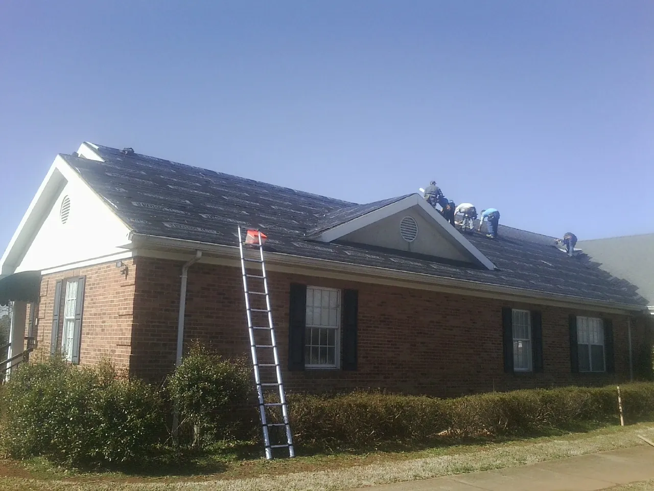 Crew tearing shingles off a brick ranch roof with a ladder set — Emergency Roof Repair work by our crew in Holtwood
