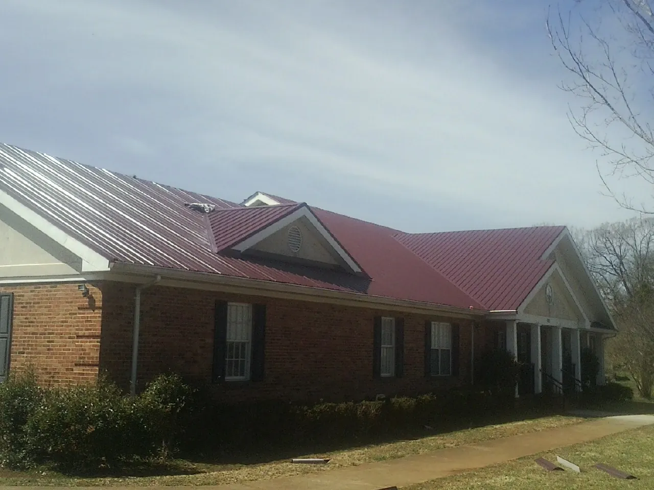 Red metal roof with gabled entries on a long brick building, from a Hail Damage Roof Repair job in Holtwood
