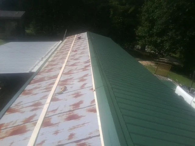 Old rusted panels beside newly installed green metal roofing — Wind Damage Roof Repair by Roofing Brothers in Holtwood