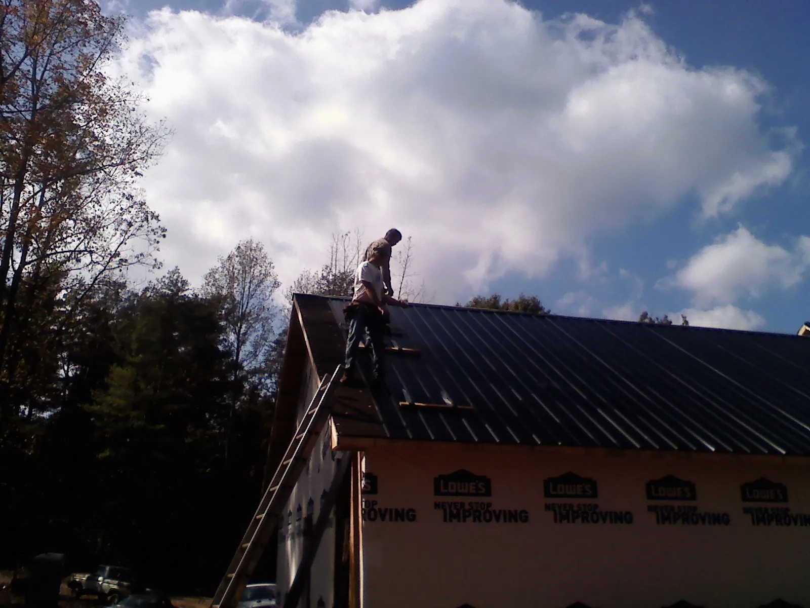 Roofer fastening dark metal panels high against a cloudy sky, from a Roof Inspection job in Holtwood