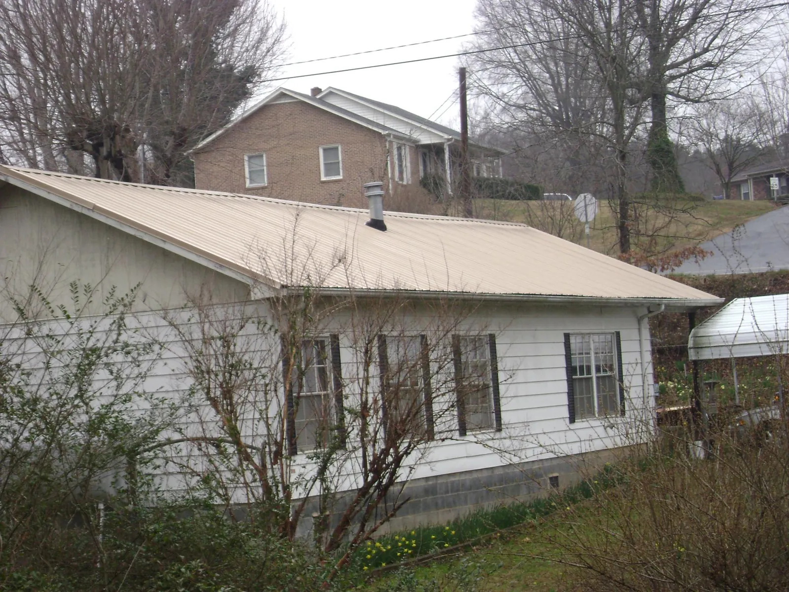 Tan metal roof on a white sided house set into a hillside — Commercial Roofing by Roofing Brothers in Holtwood